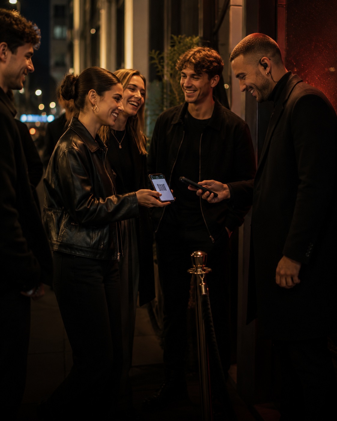 Eine Gruppe steht nachts vor einem Club-Eingang, zeigt Tickets auf dem Smartphone und lächelt.